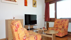 A living room with a flat-screen TV, two patterned armchairs, a wooden cabinet, and a small table. - Nice Apartment Near Ski-lift (Veysonnaz)