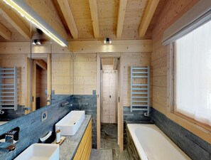 Ein modernes Badezimmer mit Holzwänden, einem großen Spiegel, einer Badewanne und einem Doppelwaschbecken.