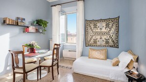 A bedroom with a bed, a desk with chairs, a window with curtains, and a wall-mounted tapestry.