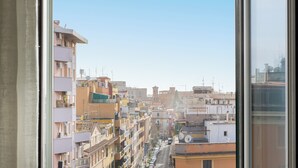 A view of a densely packed urban street with multi-story buildings, some with balconies, and a clear sky.