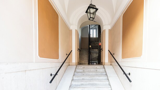 A staircase with marble steps and black handrails, leading to a door with a metal gate.