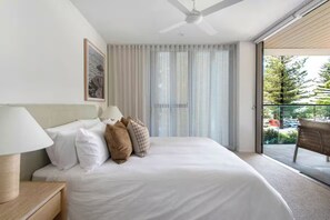 A bedroom with a bed, a nightstand, a ceiling fan, a window with blinds, and a view of the outdoors. - Luxury Villas Burleigh Bliss (Ocean Views) (Burleigh Heads)