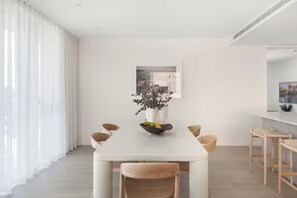 A modern dining area with a white table, wicker chairs, a vase with flowers, and a framed picture on the wall. - Luxury Villas Burleigh Bliss (Ocean Views) (Burleigh Heads)