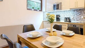 A modern kitchen with white cabinets, a microwave, and a coffee machine. There is a dining table with four chairs and a vase with flowers. - Comfortable Villa With Amenities (Harrachov)