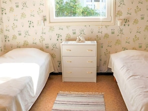 A bedroom with two beds, a nightstand, a window with a view, and a striped rug.