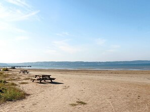 A beach with picnic tables and a pier in the background.