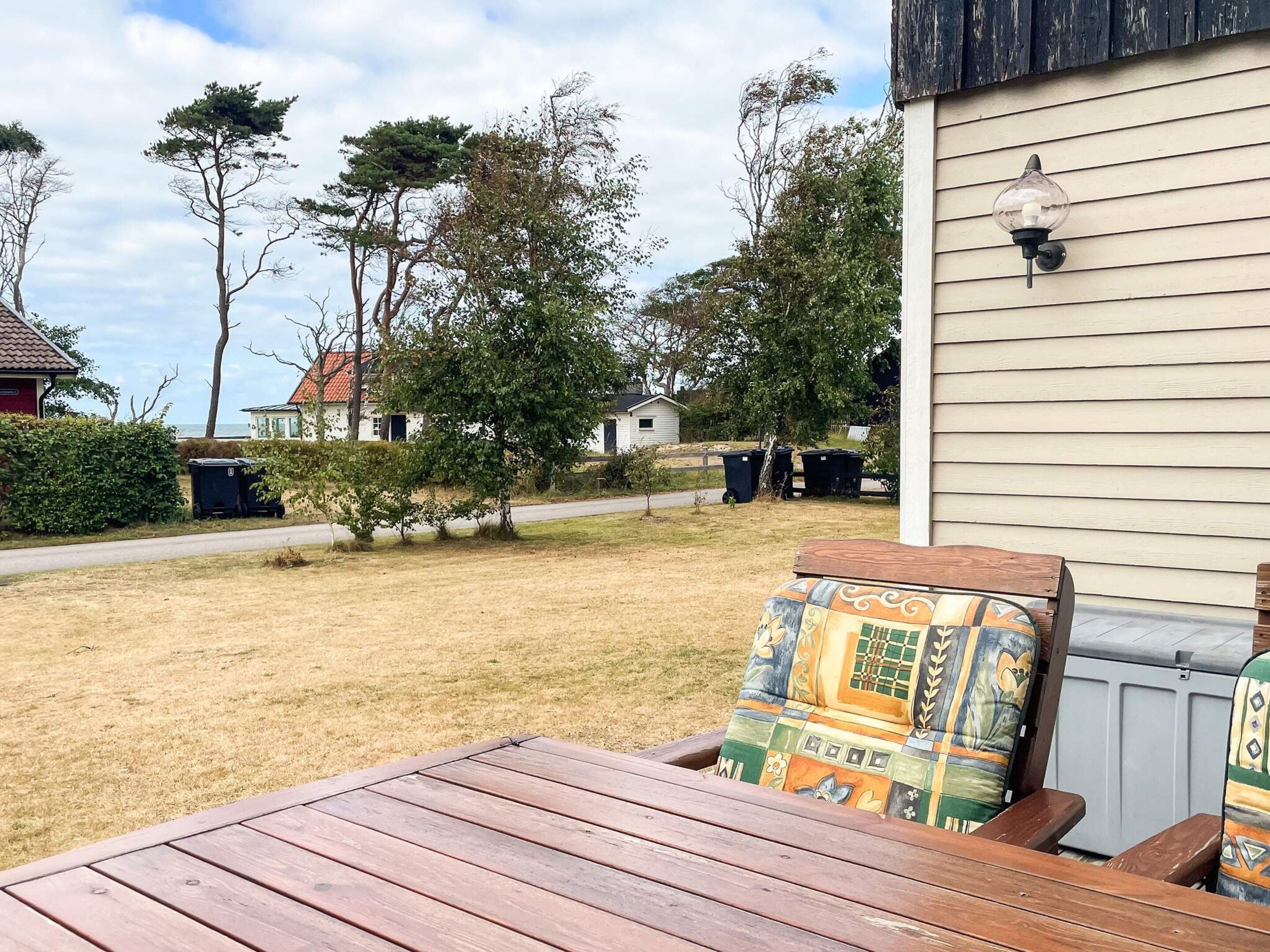 A wooden deck with a table and chairs, a house with siding, and a clear sky.
