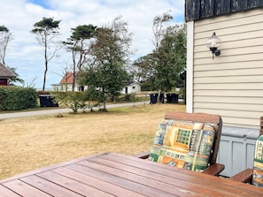 A wooden deck with a table and chairs, a house with siding, and a clear sky.