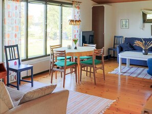 A living room with a dining table, chairs, a sofa, a TV, and a window with curtains.