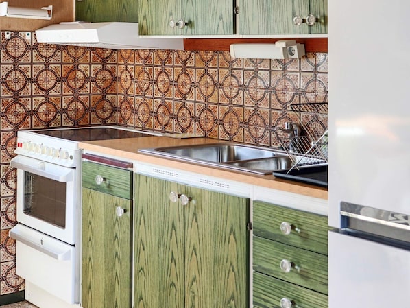 A kitchen with green cabinets, a stainless steel sink, and a white stove.