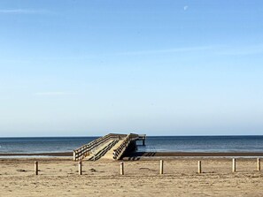 A beach with a wooden staircase leading to a pier.