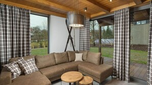 Una sala moderna con un sofá modular, dos mesas redondas de madera y cortinas a cuadros.