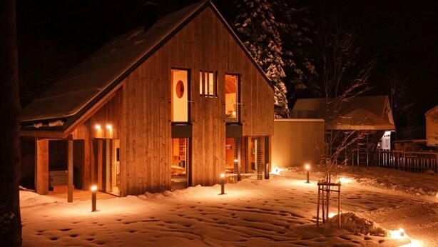 Un edificio de estilo granero de madera con techo inclinado, ventanas grandes y suelo cubierto de nieve.