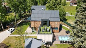 Una casa moderna con una terraza amplia, piscina y un coche aparcado cerca.