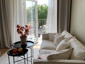 A living room with a white sofa, a small round table with a potted plant, and a glass door leading to an outdoor balcony. - 4 Star Holiday Home in Solvesborg (Sölvesborg)