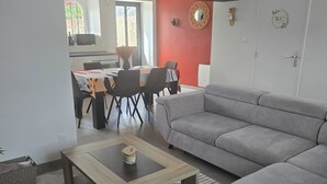 A modern living room with a grey sofa, a coffee table, and a dining area with chairs and a table. - Charming family home with garden (Château-Gontier-sur-Mayenne)