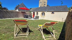 A grassy outdoor area with two wooden chairs and a red umbrella. In the background, there is a building with a tower and a clock. - Charming family home with garden (Château-Gontier-sur-Mayenne)