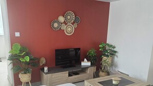 A modern living room with a red accent wall, a flat-screen TV, a wooden coffee table, and two large grey sofas. - Charming family home with garden (Château-Gontier-sur-Mayenne)