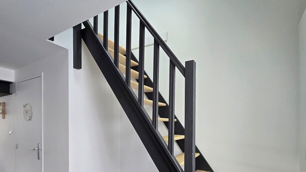 A modern staircase with black railings and wooden steps, leading to a room with a white door and a small window. - Charming family home with garden (Château-Gontier-sur-Mayenne)