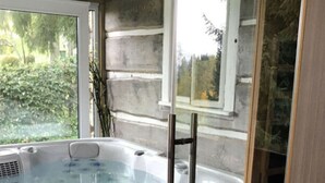 A hot tub with a glass enclosure, a wooden stool, and a window with a view of greenery. - Holiday Villa for Families (Tanvald)