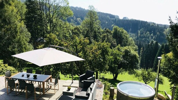 An outdoor patio with a table and chairs, a large umbrella, a hot tub, and a view of a forested hillside. - Holiday Villa for Families (Tanvald)