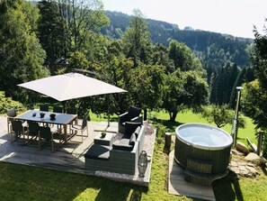 An outdoor patio with a table and chairs, a large umbrella, a hot tub, and a view of a forested hillside. - Holiday Villa for Families (Tanvald)