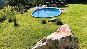 A backyard with a swimming pool, surrounded by grass and rocks. - Holiday Villa for Families (Tanvald)