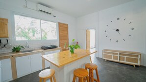 A modern kitchen with a wooden island, bar stools, a large wall clock, and a window with a view of greenery. - Villa Sawah Prambanan (Prambanan)