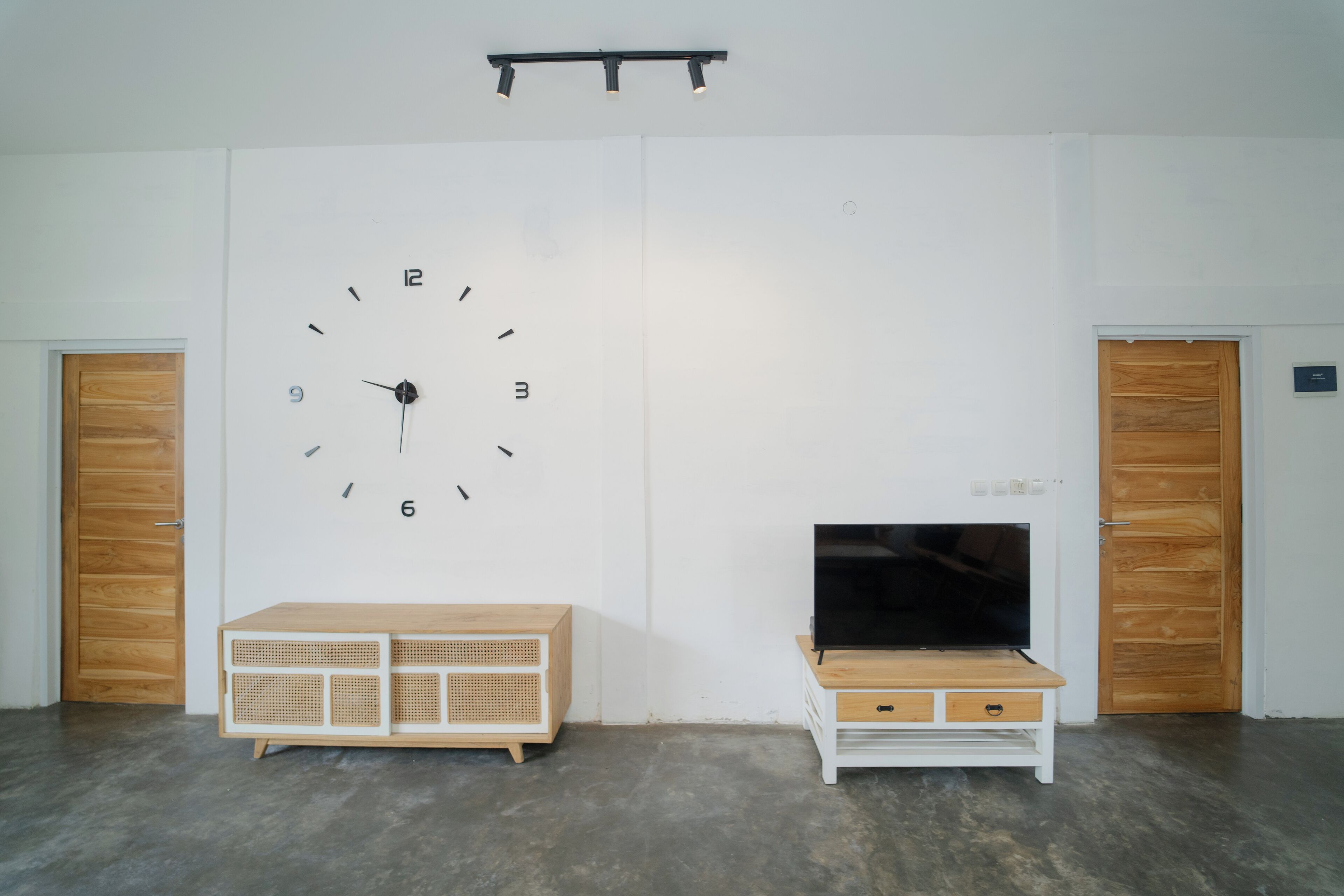 A room with a large wall clock, two wooden doors, a television on a wooden stand, and a white cabinet.