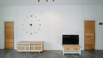 A room with a large wall clock, two wooden doors, a television on a wooden stand, and a white cabinet.