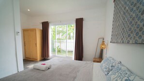 A bedroom with a large bed, a wooden wardrobe, a window with curtains, and a bedside table with a lamp. - Villa Sawah Prambanan (Prambanan)