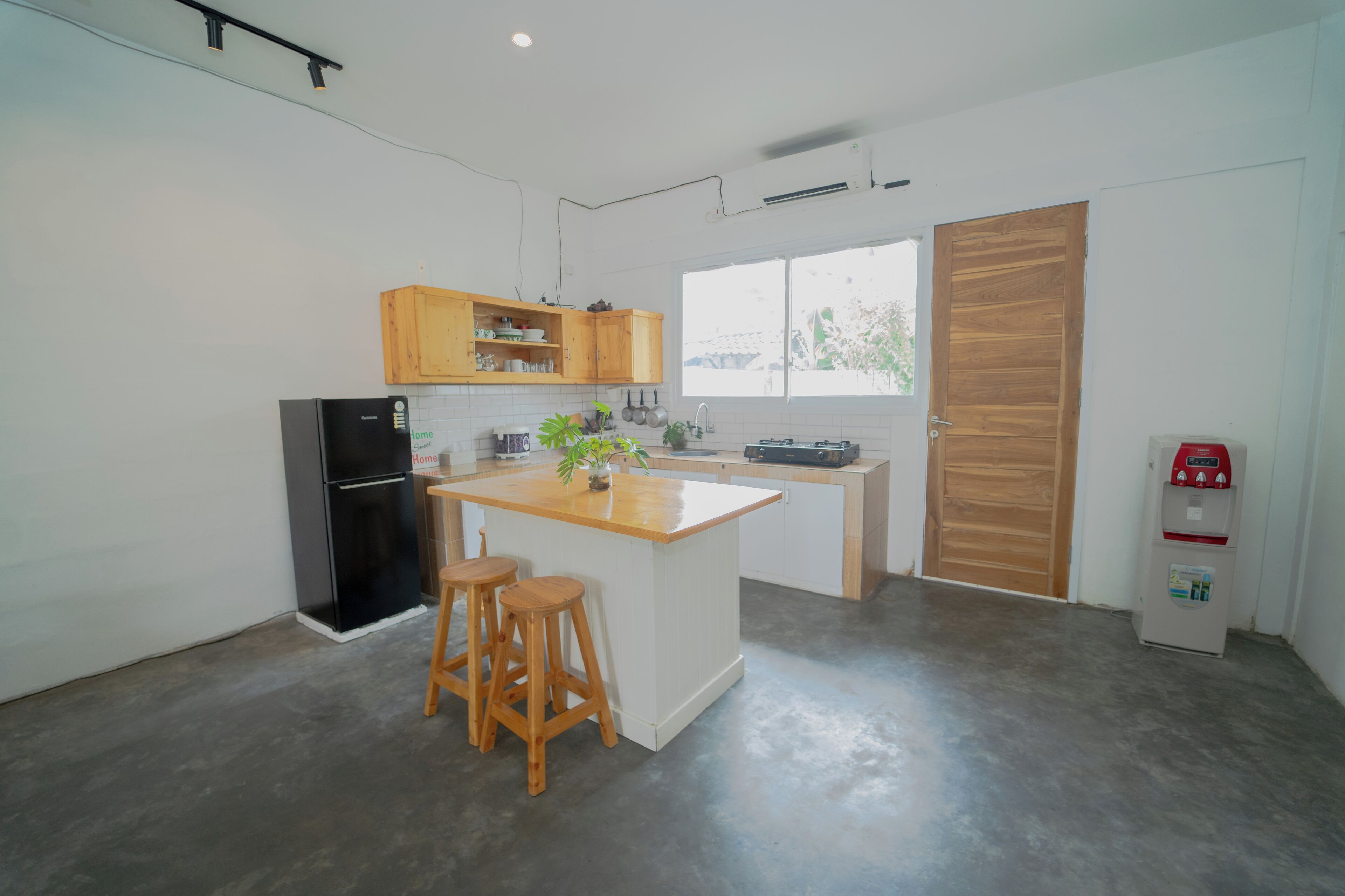 A modern kitchen with wooden cabinets, a black refrigerator, a wooden island with stools, and a window providing natural light.