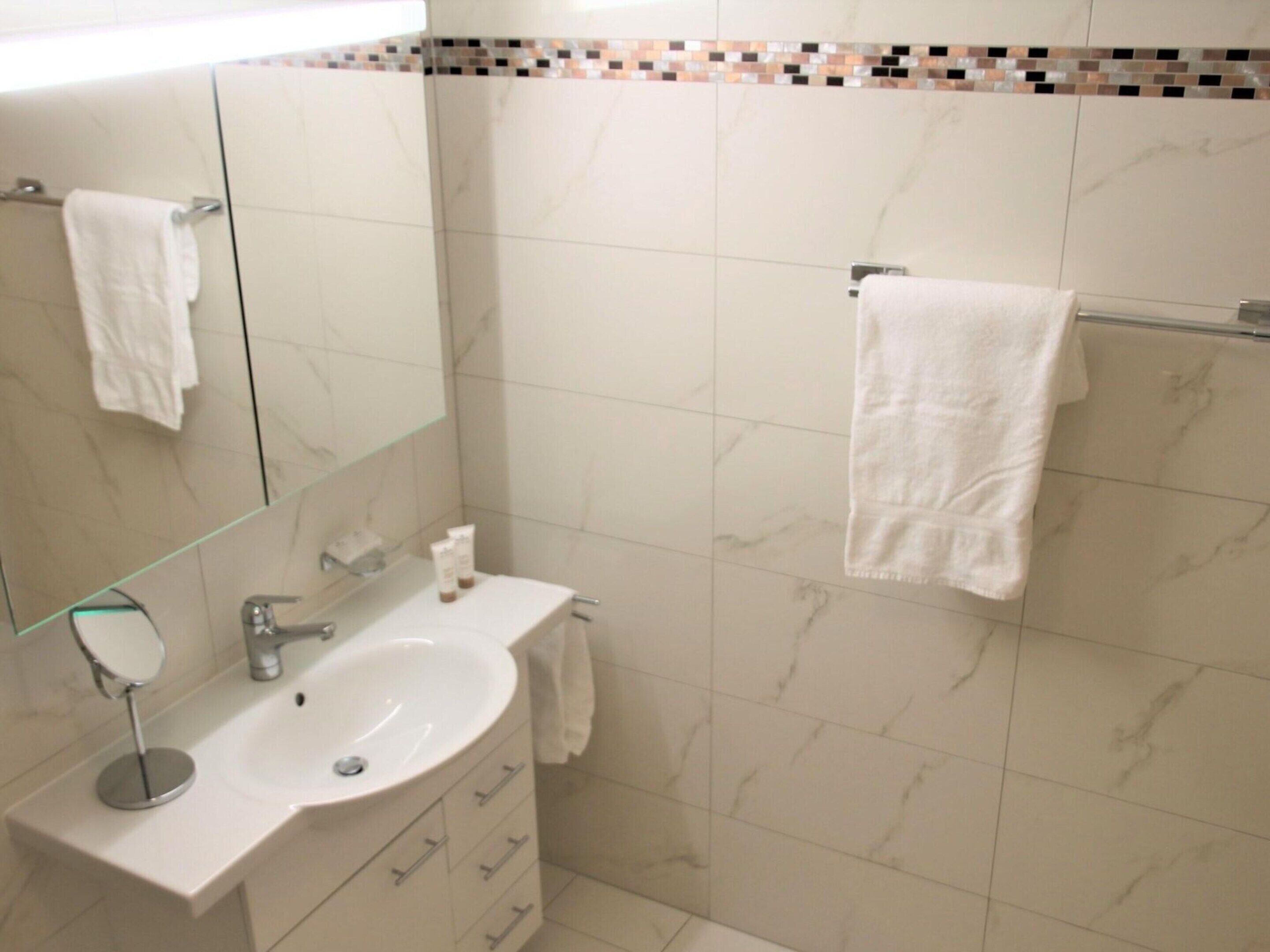 Un bagno con un lavandino bianco, uno specchio e un portasciugamani.