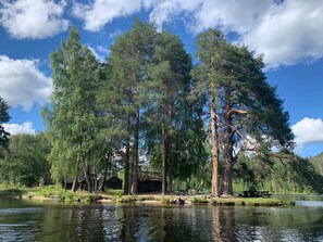 A serene lakeside setting with tall trees, a wooden cabin, and a picnic table by the water. - 3 Person Holiday Home in Graninge (Graninge)