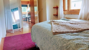 Une chambre à coucher avec un lit, une fenêtre avec des rideaux, une porte donnant sur une autre pièce et une petite table avec des chaises.