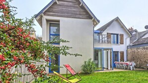 Una casa de dos pisos con techo inclinado, patio trasero cercado y un pequeño patio con mobiliario exterior.