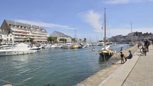 Un puerto deportivo con barcos amarrados, un paseo marítimo y edificios al fondo.