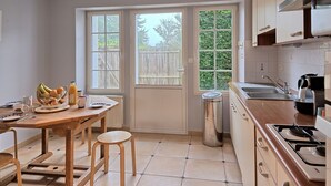Una cocina con una mesa de madera, taburetes, un cubo de basura y una estufa.