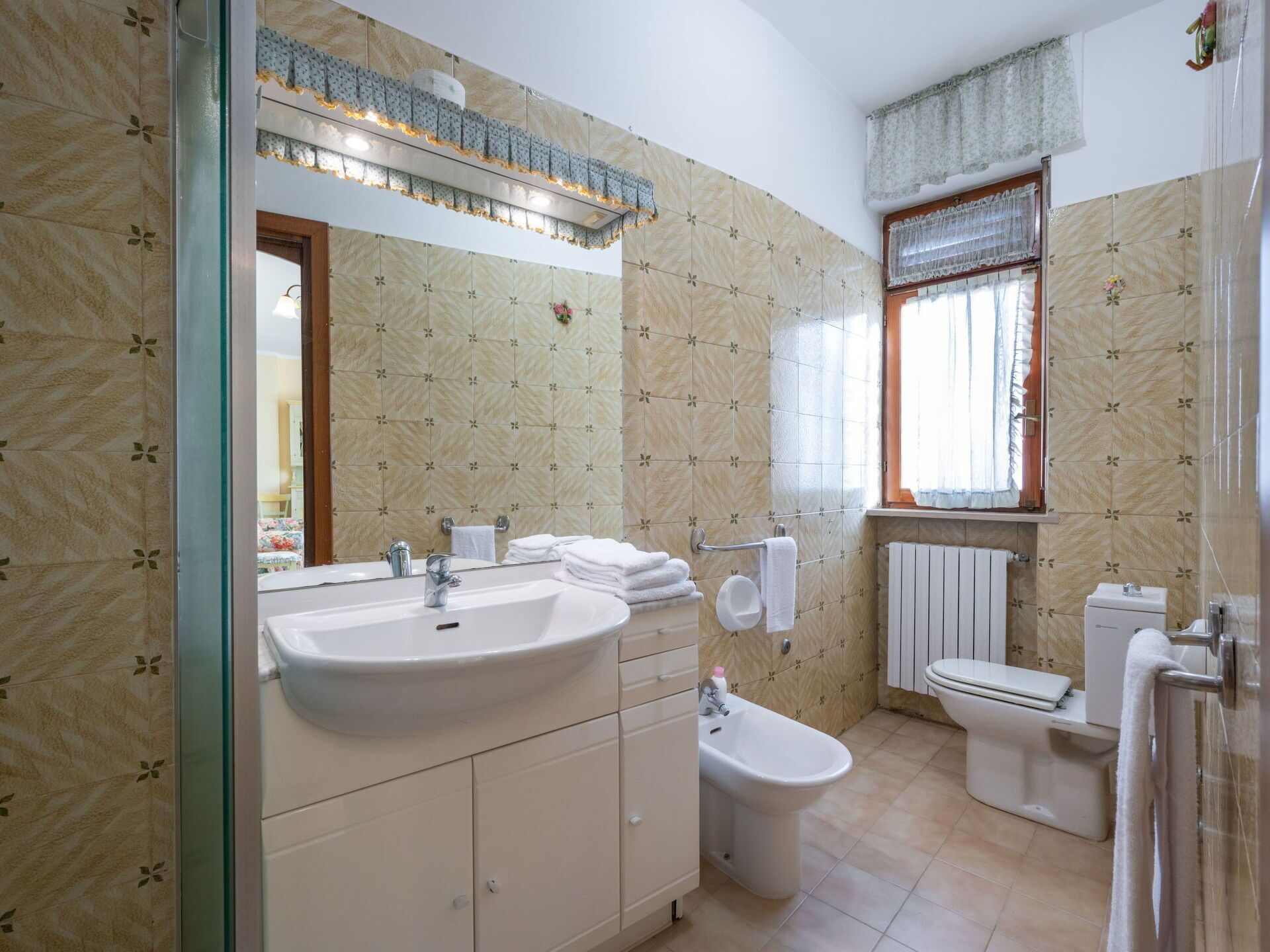A bathroom with a large sink, a bidet, a toilet, and a window with curtains.