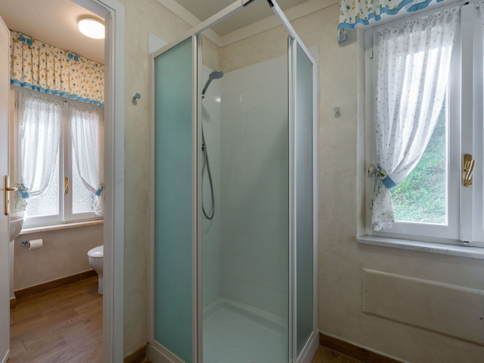 Une salle de bain avec une douche à parois de verre, des toilettes et une fenêtre avec des rideaux.