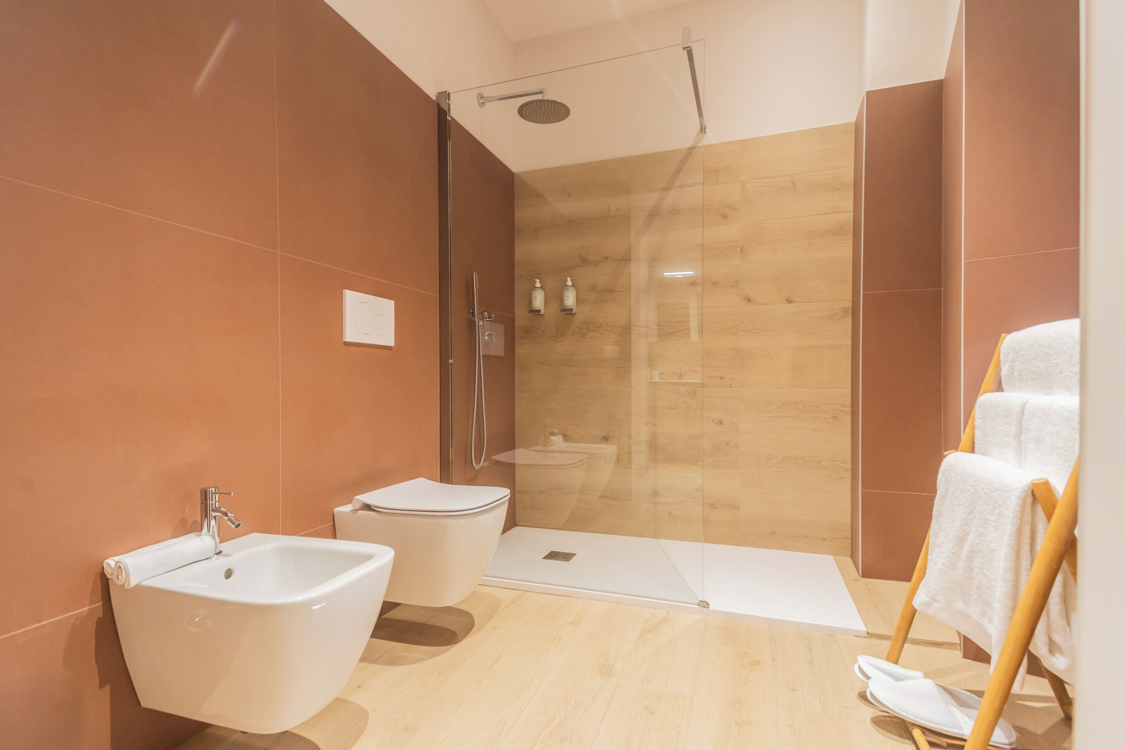 Un baño moderno con bidé, inodoro, zona de ducha y perchero para toallas.