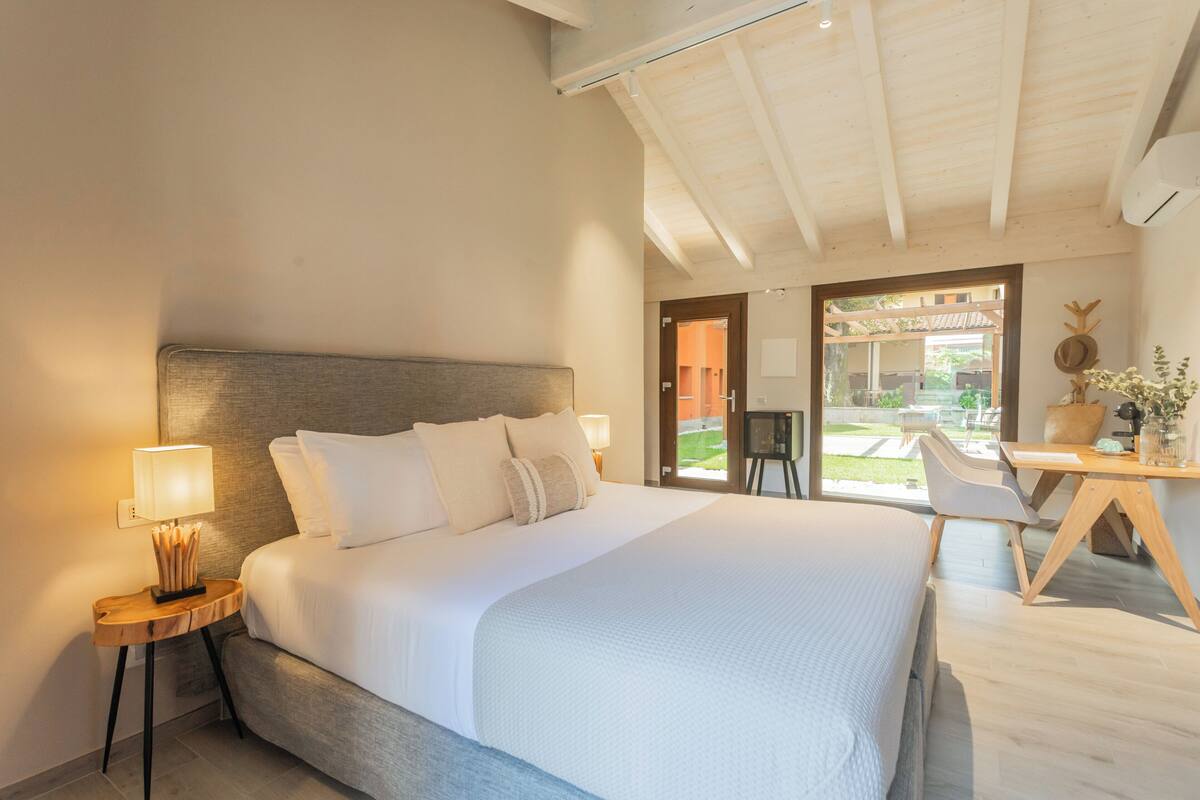 A modern hotel room with a large bed, a desk, and a view of the outdoor area.