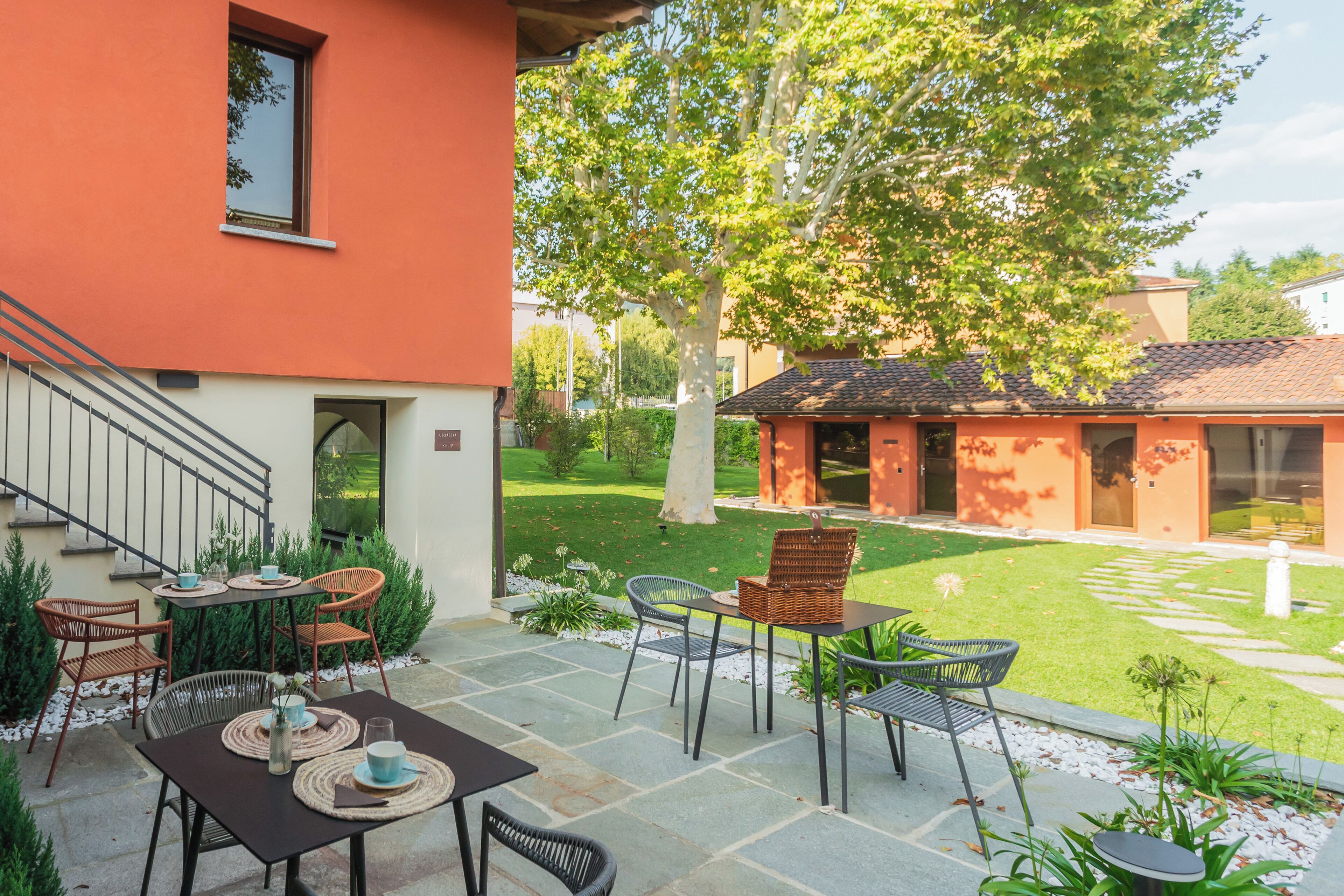 Um pátio com mobiliário externo, uma escadaria e vista para um jardim e edifícios vizinhos.