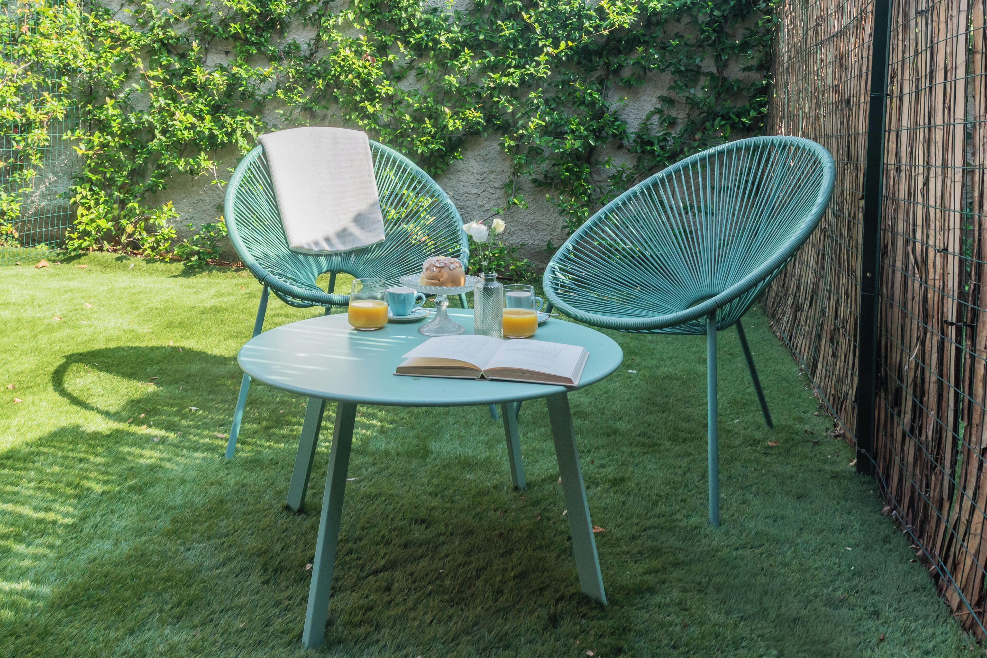 A small round table with two chairs, a book, a glass of orange juice, and a muffin.