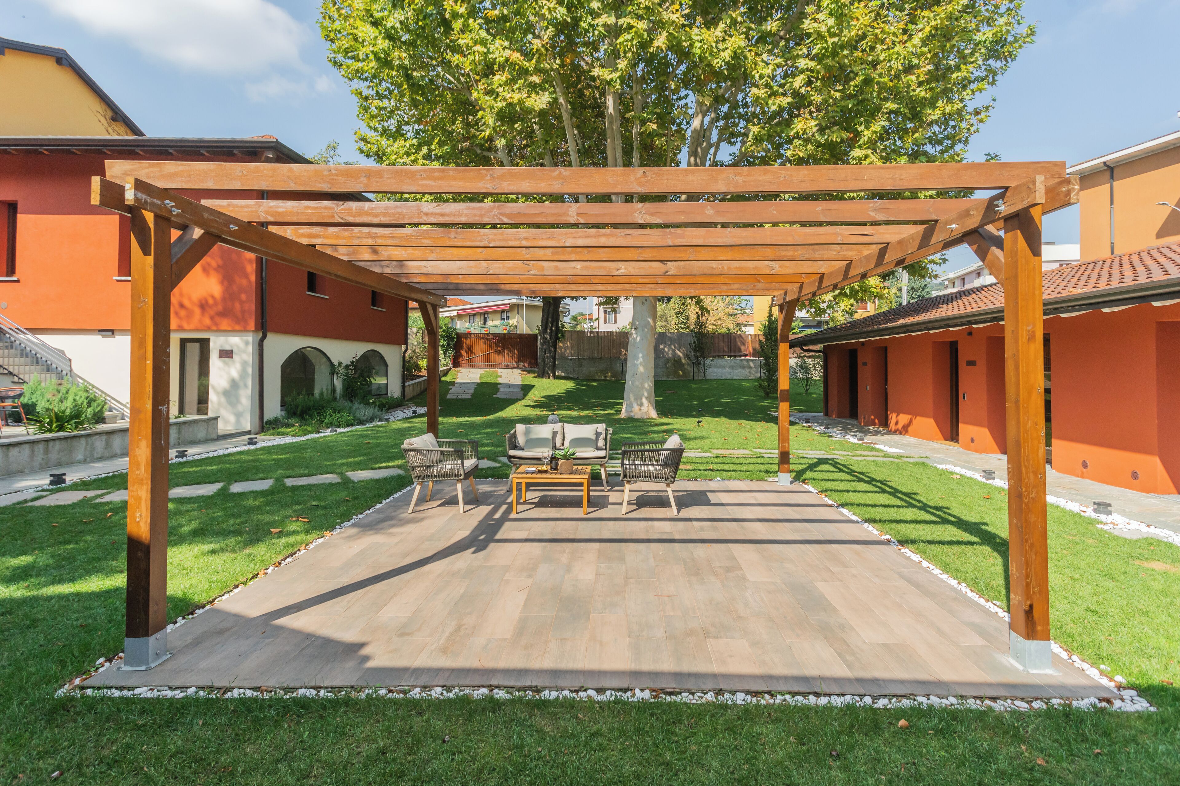 An outdoor patio area with a wooden pergola, a seating arrangement with two sofas and a coffee table, and a well-maintained lawn.