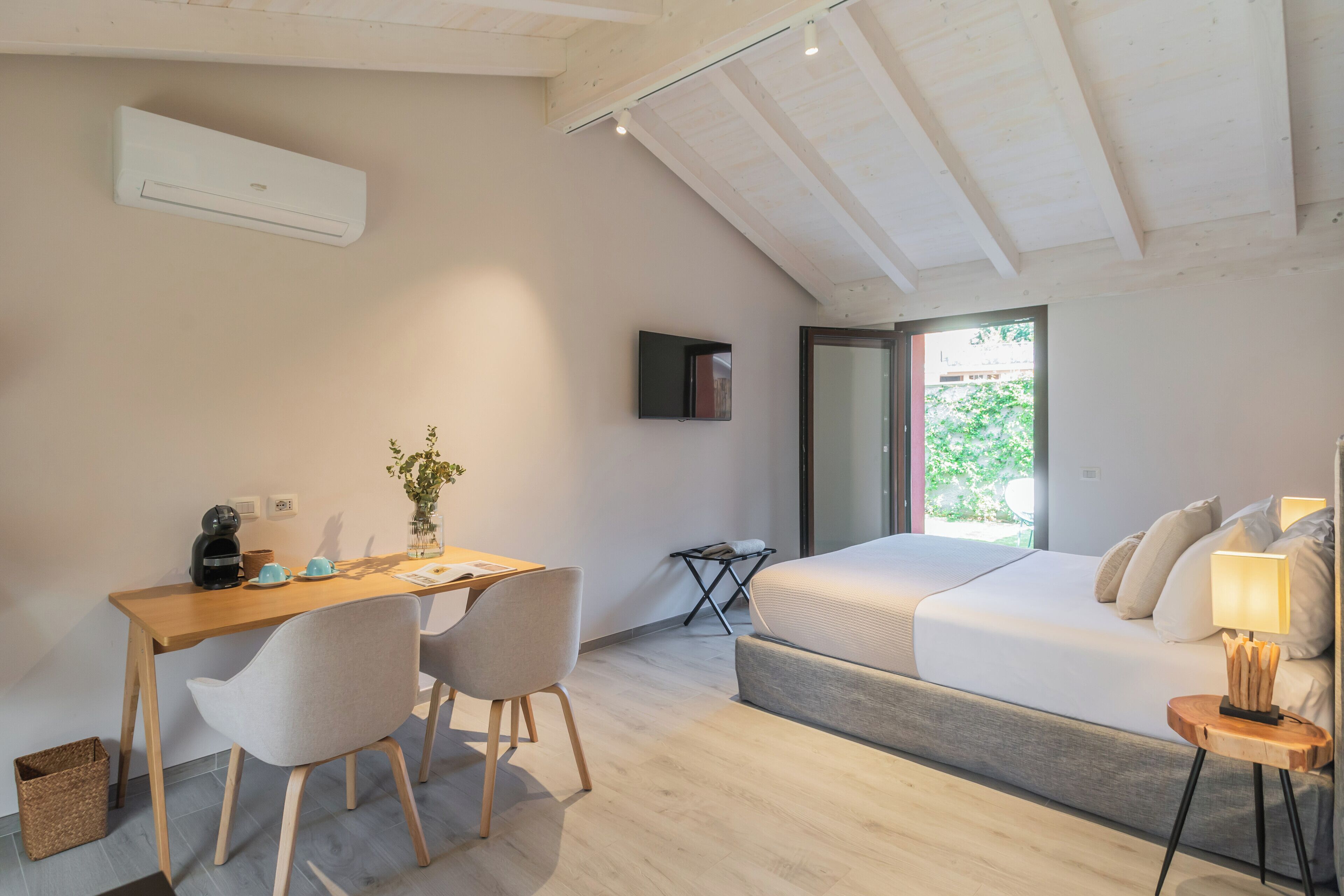 A modern bedroom with a bed, bedside table, lamp, and a desk with chairs.