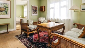 Une pièce avec une table en bois, des chaises en osier, un canapé, un tapis à motifs et une grande fenêtre ornée de rideaux légers.