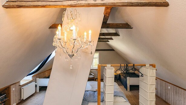Une chambre confortable située sous les toits, avec un lustre, des poutres en bois et un lit en mezzanine.