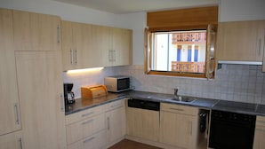 Eine moderne Küche mit hellen Holzschränken, einer eingebauten Mikrowelle und einem Fenster mit Blick auf einen Balkon.