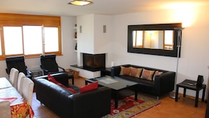 Ein Wohnzimmer mit einer Couch, Sesseln, einem Couchtisch, einem Fernseher und einem Kamin.